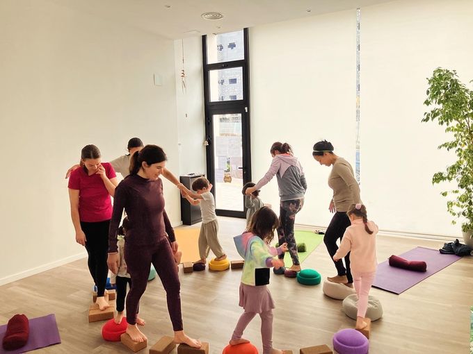 Personas y niños practicando el equilibrio sobre bloques en un estudio de yoga.