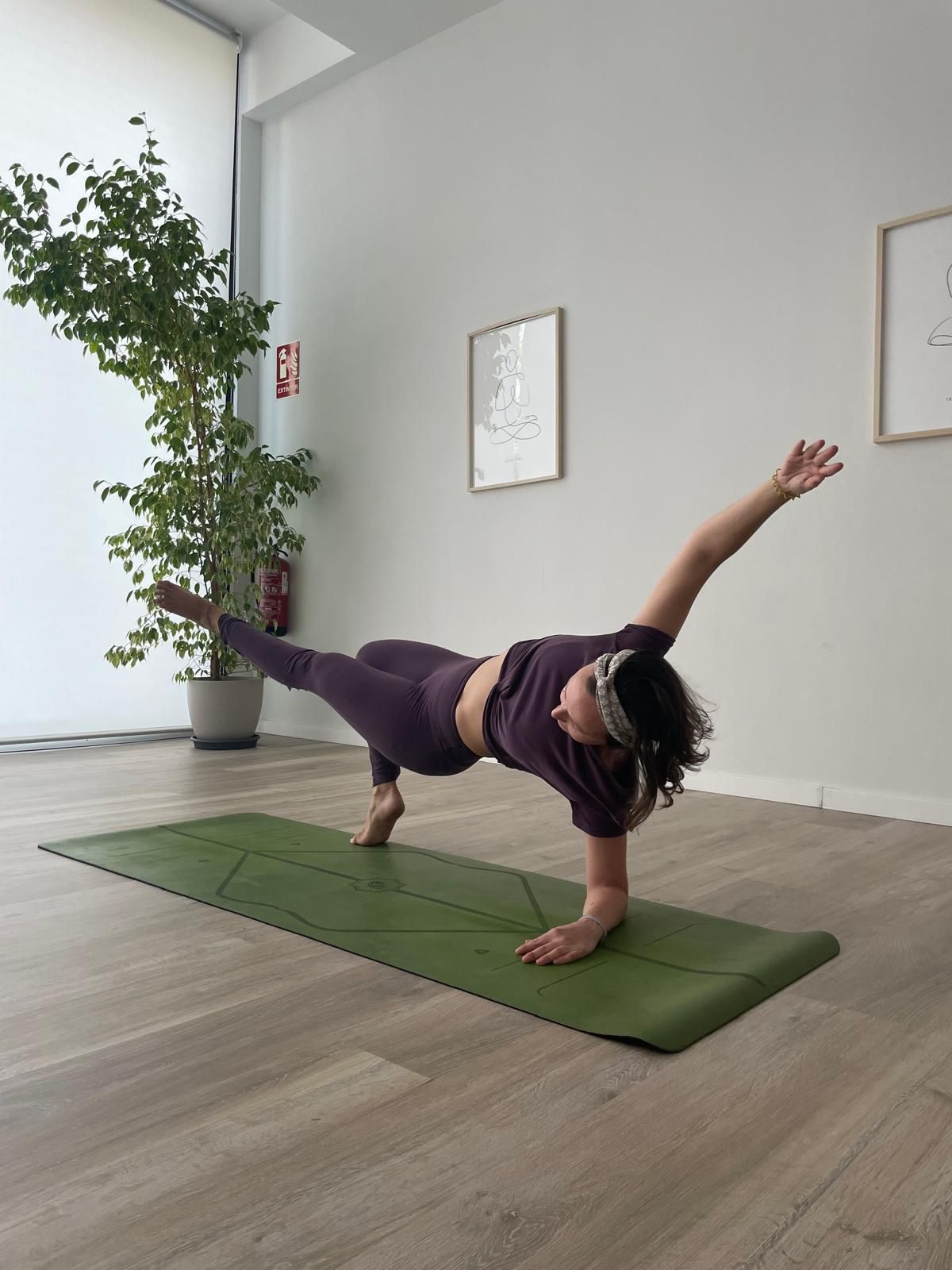 Mujer con traje de yoga morado haciendo una estocada lateral sobre una colchoneta verde