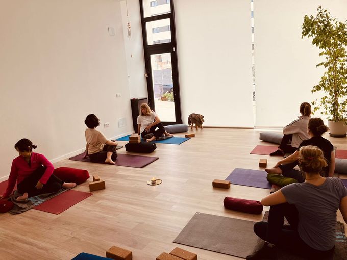 Personas en una clase de yoga, sentadas en colchonetas, con un profesor, en un estudio lleno de luz.