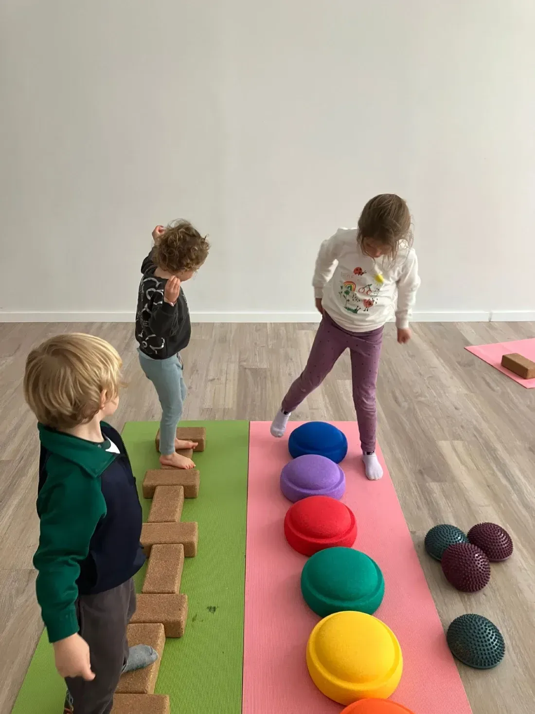 Niños haciendo equilibrio sobre ladrillos y piedras en una habitación llena de luz.