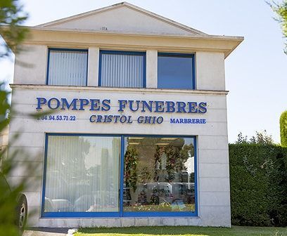 Maison funéraire Pompes Funèbres Cristol Ghio, bâtiment clair avec garnitures et enseigne bleues.