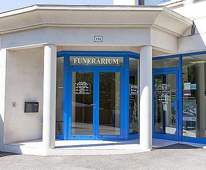 Extérieur d'un funérarium avec une entrée bleue, des portes vitrées et des colonnes blanches.