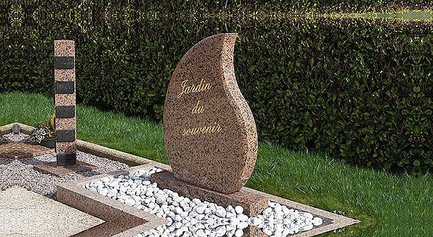 Pierre tombale en forme de flamme dans un jardin. Pilier beige et noir à gauche.