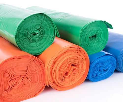 Rollos de bolsas de plástico de diferentes colores se apilan uno encima del otro sobre una superficie blanca.