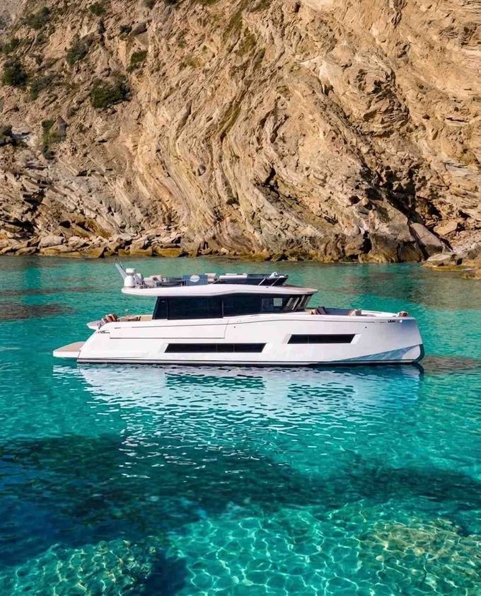 Yate a motor blanco sobre aguas de color turquesa brillante junto a un acantilado rocoso.