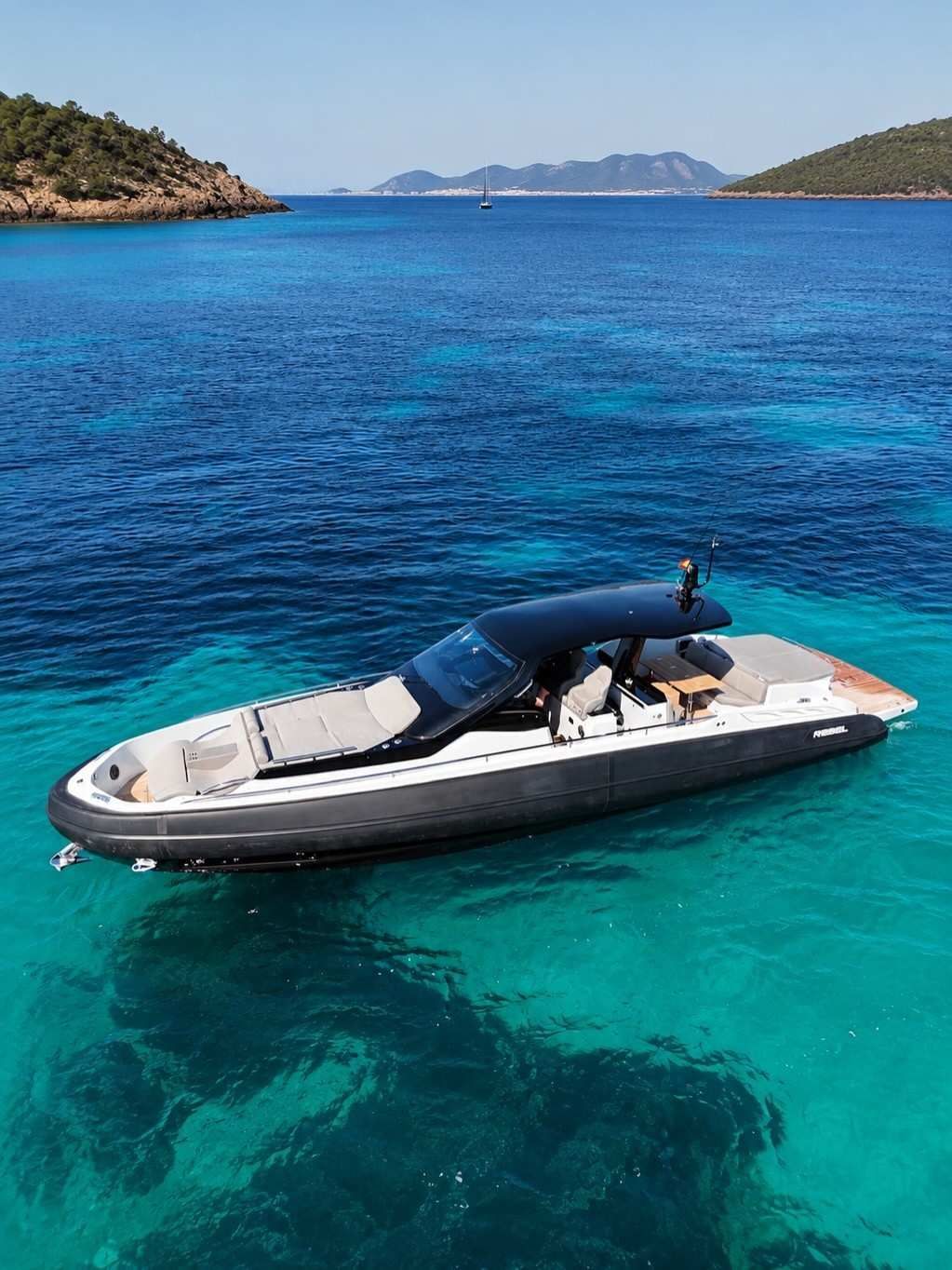 Un elegante yate a motor blanco y negro en aguas cristalinas cerca de islas rocosas bajo un cielo soleado.