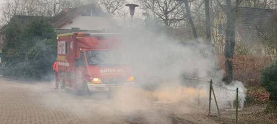 Ein Feuerwehrauto fährt eine Straße entlang und aus ihm steigt Rauch auf.