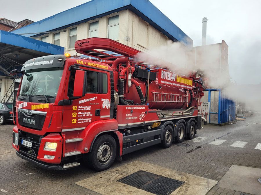 Ein roter Saugwagen steht vor einem Gebäude.