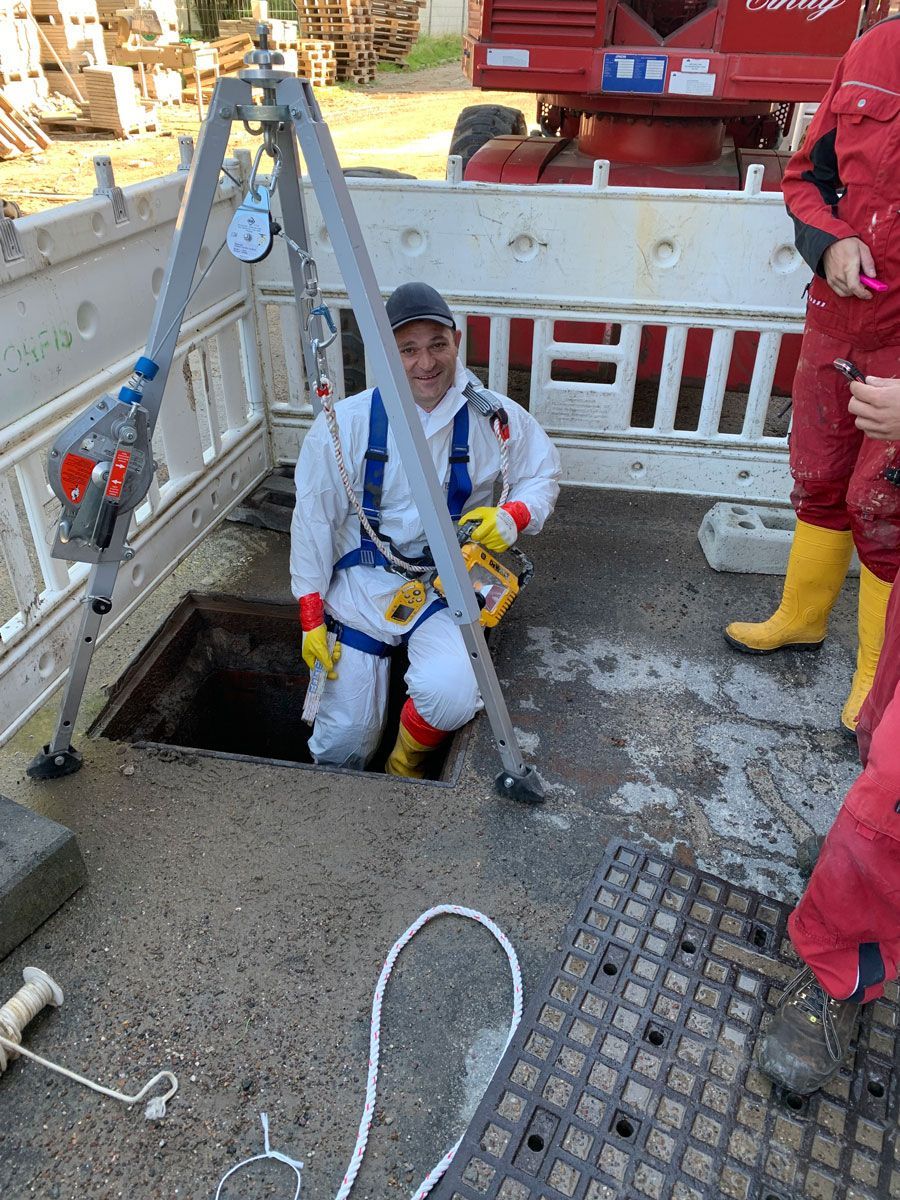 Ein Mann im weißen Anzug sitzt in einem Kanaldeckel.