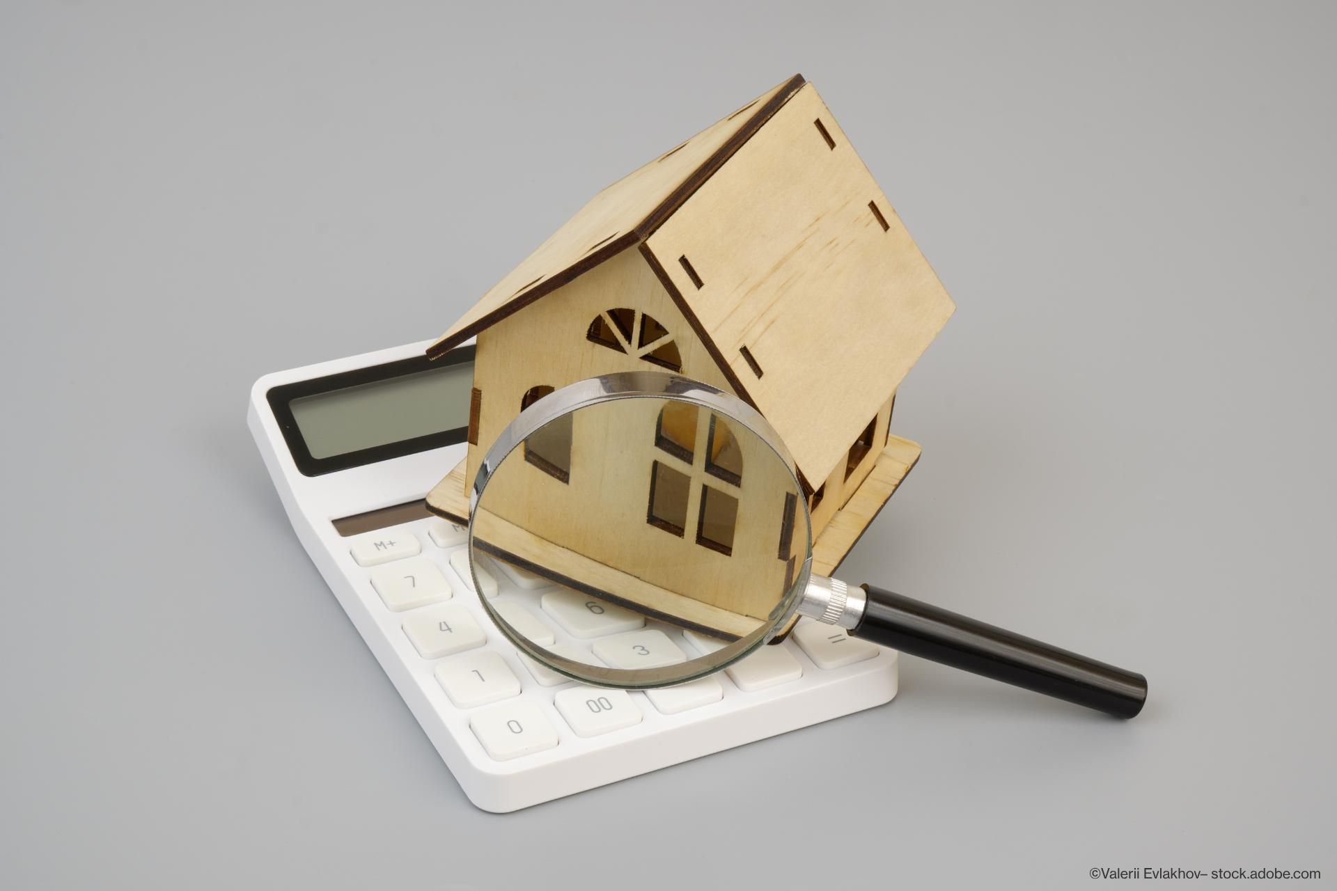 Holzmodell eines Hauses mit einer Lupe, die auf einem Taschenrechner liegen