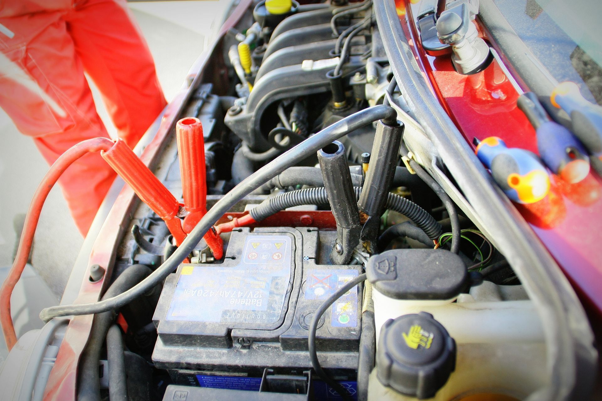 Compartiment moteur de voiture avec câbles de démarrage connectés à une batterie ; câbles rouges, une combinaison rouge.