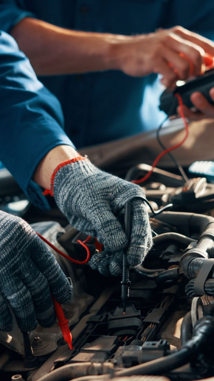 Des mécaniciens en combinaison bleue testent le moteur d'une voiture avec un multimètre et portent des gants.