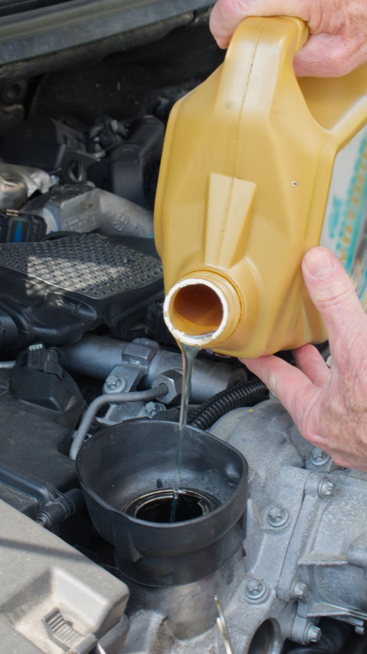 Une personne verse de l'huile dans le moteur d'une voiture à partir d'un récipient jaune.