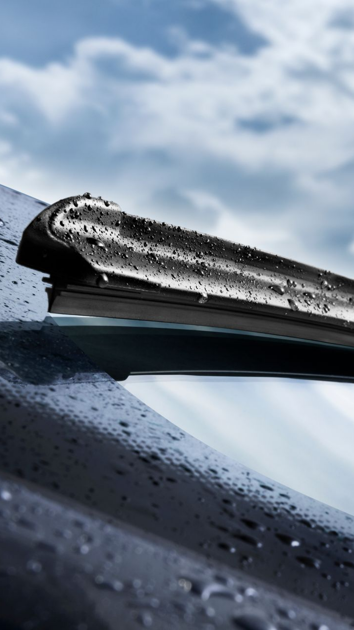 Essuie-glace d'une voiture, couvert de gouttes de pluie, sur fond de ciel nuageux.