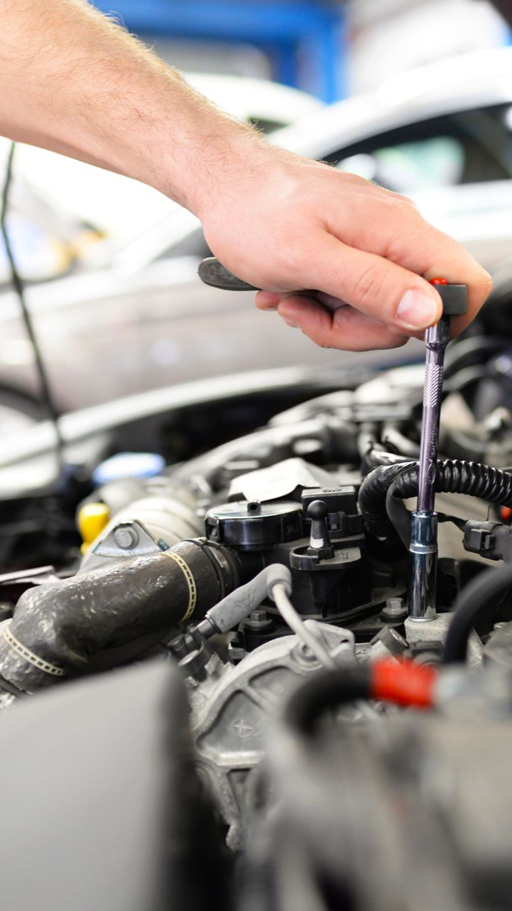 Main de mécanicien utilisant un tournevis sur un moteur de voiture dans un garage.
