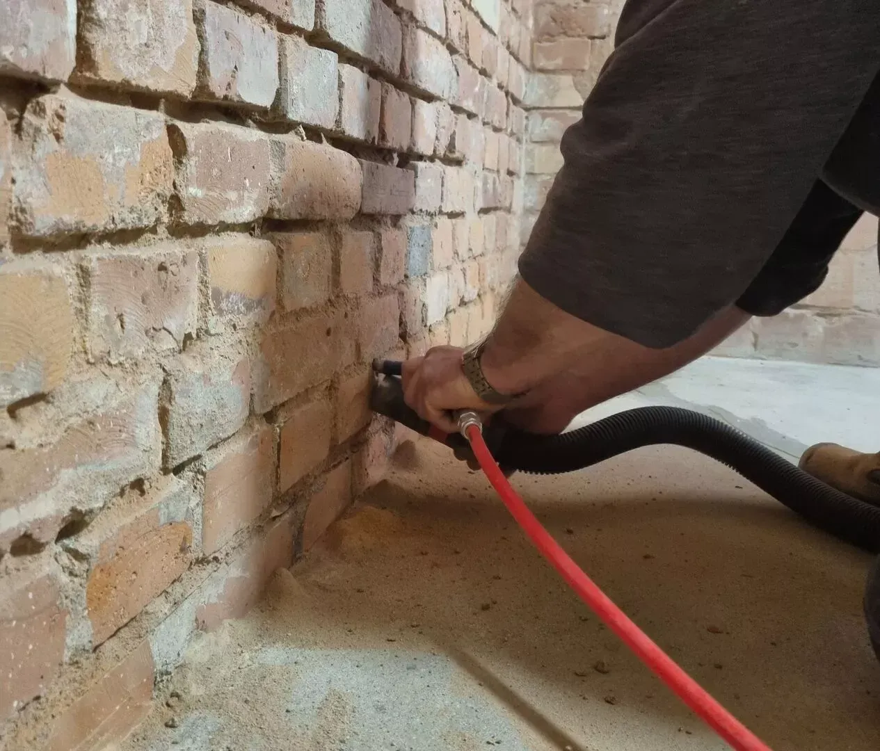 Ein Mann arbeitet mit einem roten Schlauch an einer Ziegelmauer