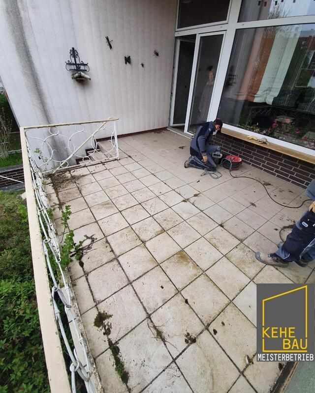 Ein Mann kniet auf einer gefliesten Veranda neben einem Gebäude.