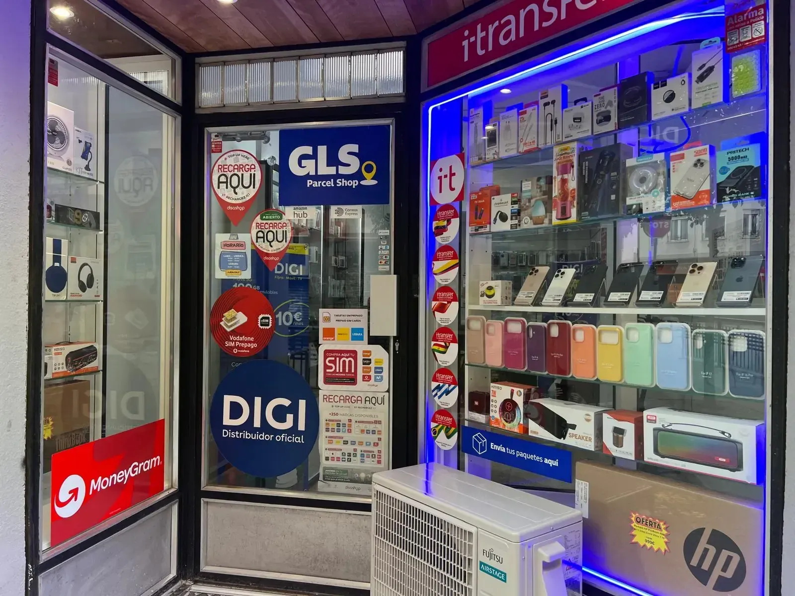 Tienda de telefonía móvil con productos expuestos en vitrinas. Incluye un cartel de envío de GLS y aire acondicionado.
