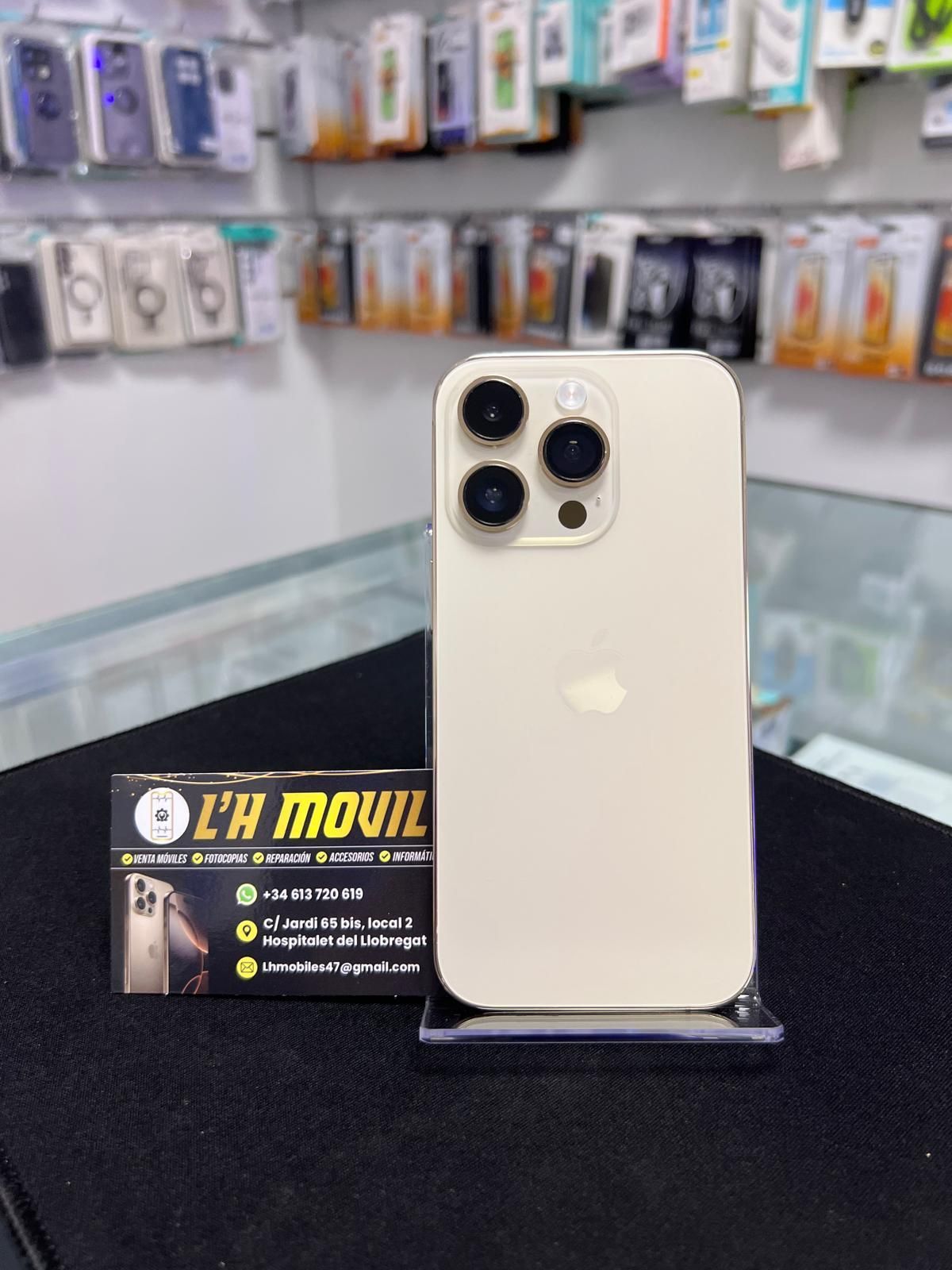 IPhone Pro en una tienda, mostrando su cámara y color dorado, con una tarjeta de presentación.