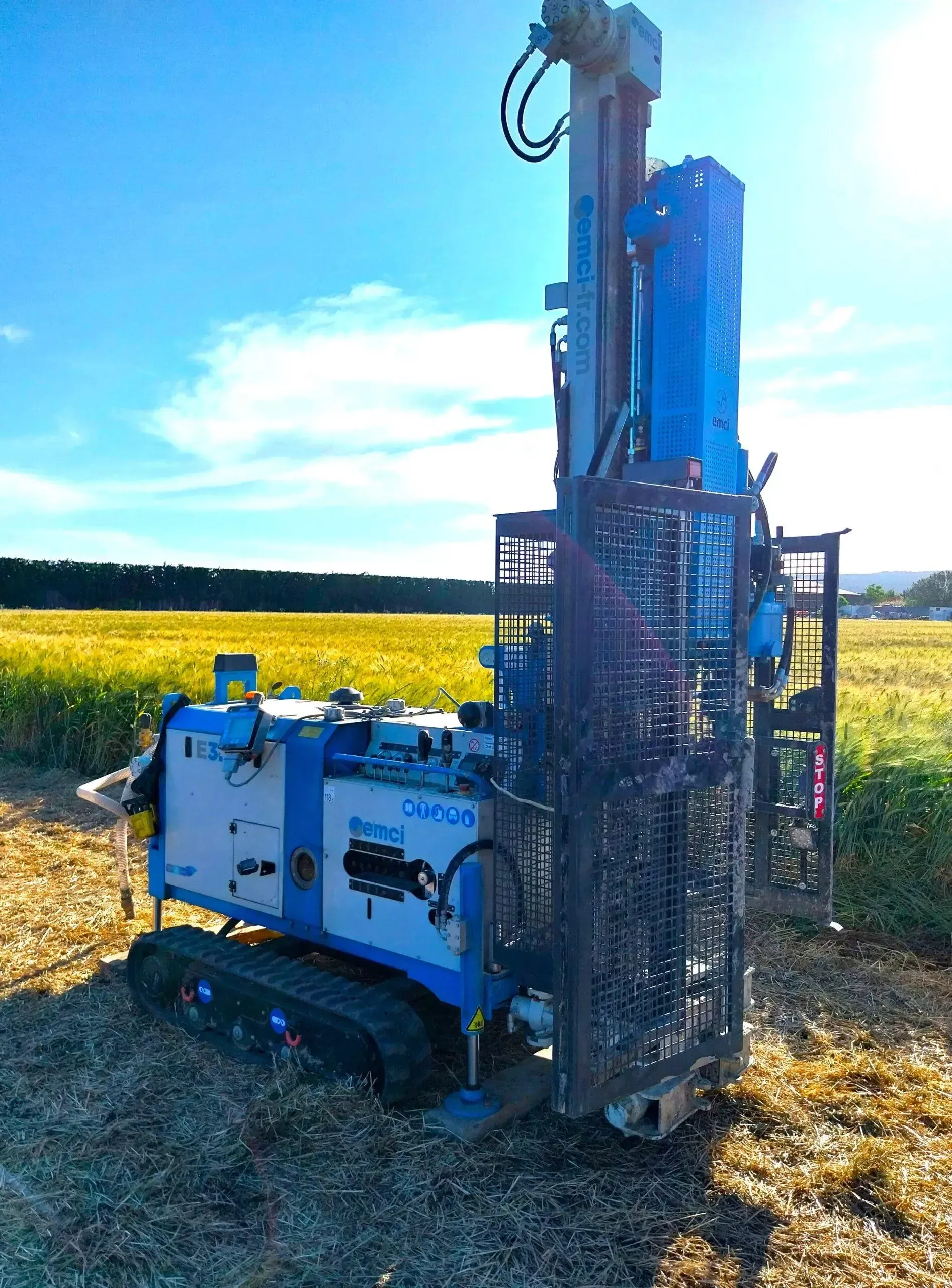 Foreuse bleue et blanche dans un champ sous un ciel ensoleillé.