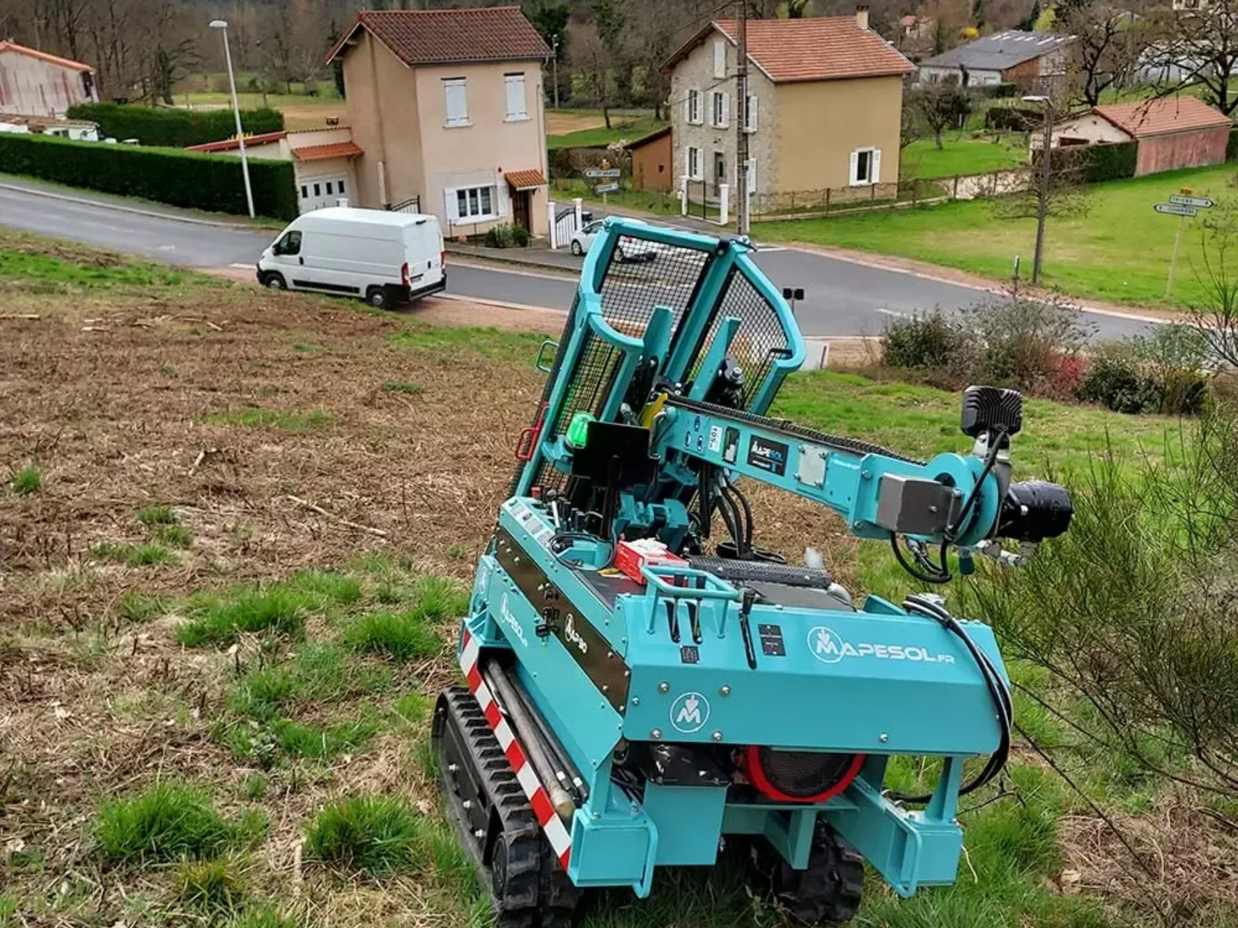 Bras robotique sur chenilles, tondant une colline herbeuse dans une zone rurale.