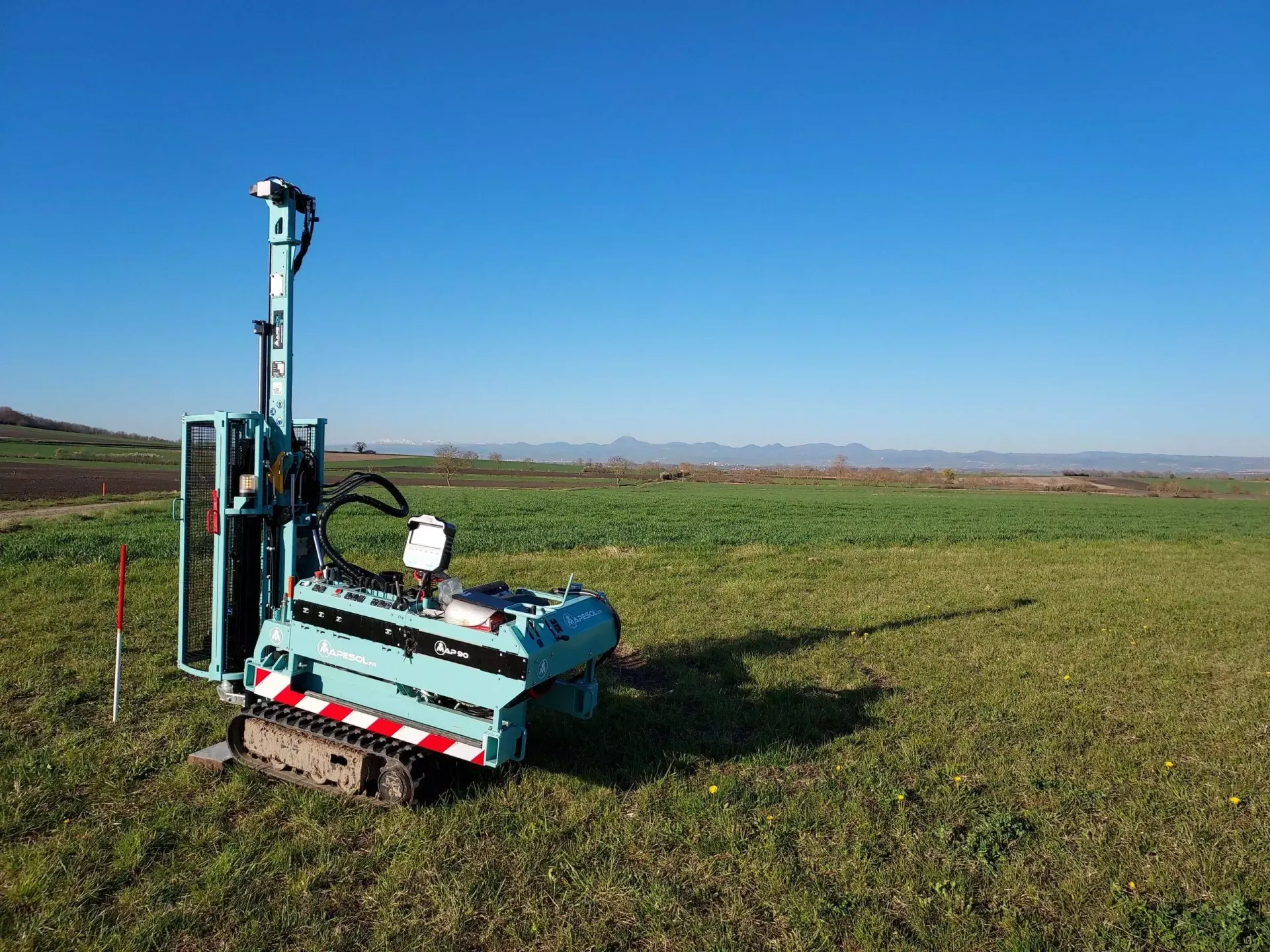 Perceuse robotisée bleue et blanche dans un champ vert sous un ciel bleu clair.