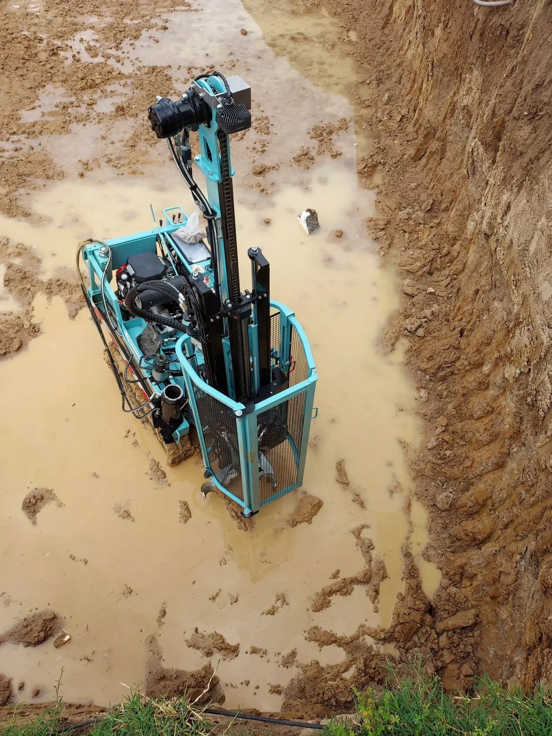 Foreuse bleue dans une excavation boueuse.