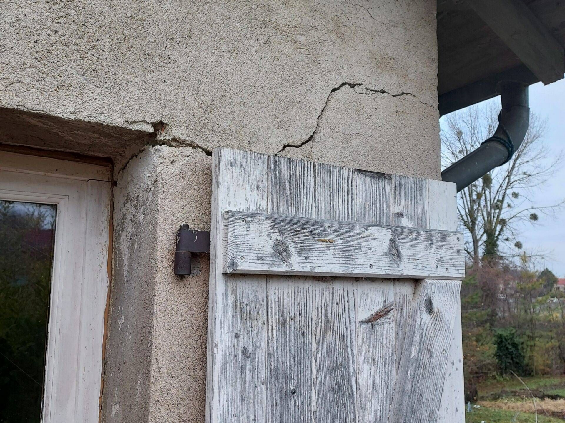 Gros plan sur la fissure présente sur la façade d'une maison avec un volet en bois.