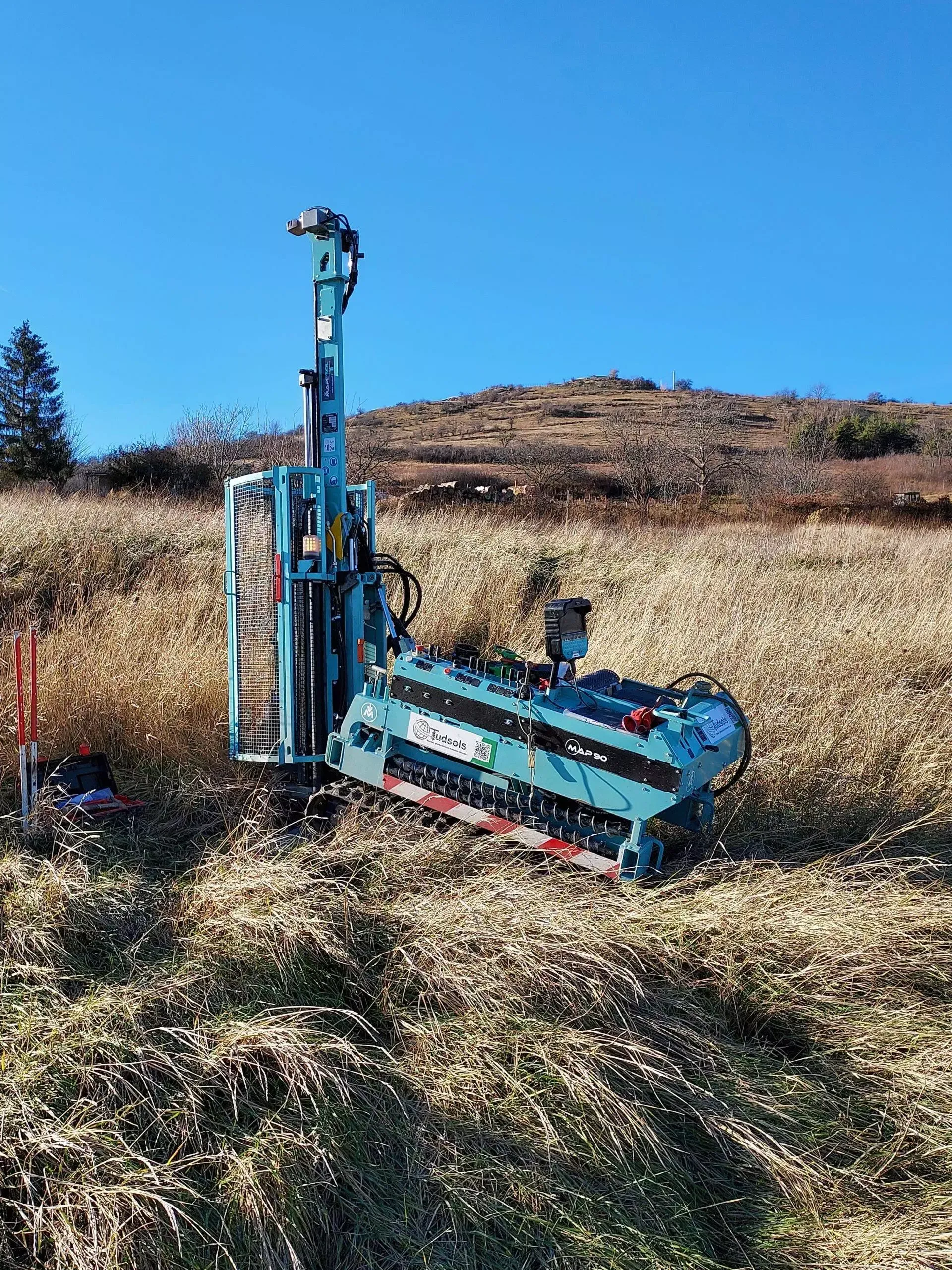 Une foreuse sarcelle sur une colline herbeuse sous un ciel bleu clair.