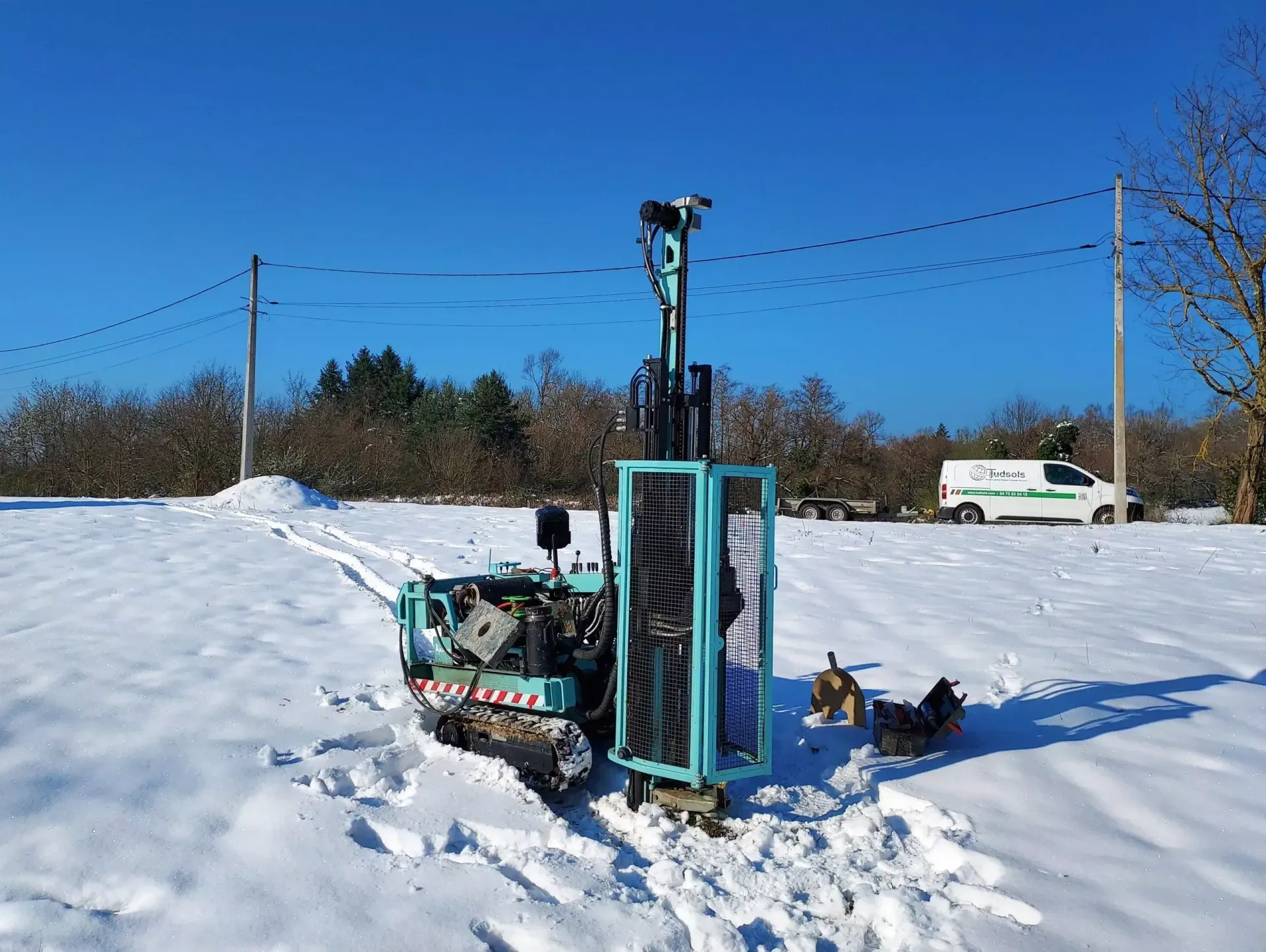 Une foreuse bleue sur chenilles dans un champ enneigé par une journée ensoleillée.