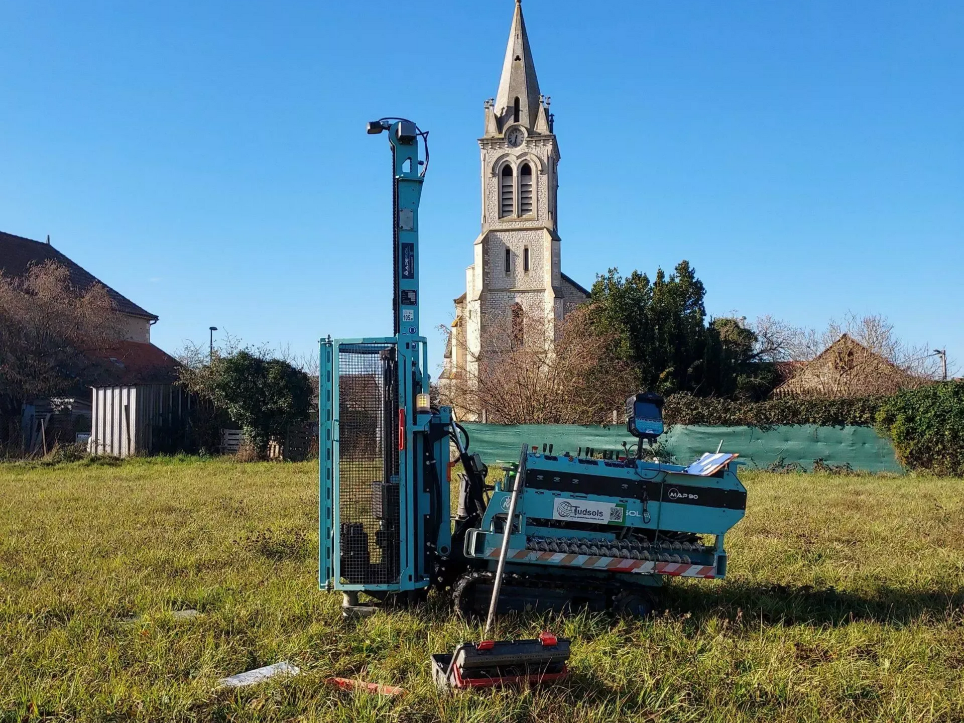 Foreuse au milieu d'un champ avec une église en arière-plan.