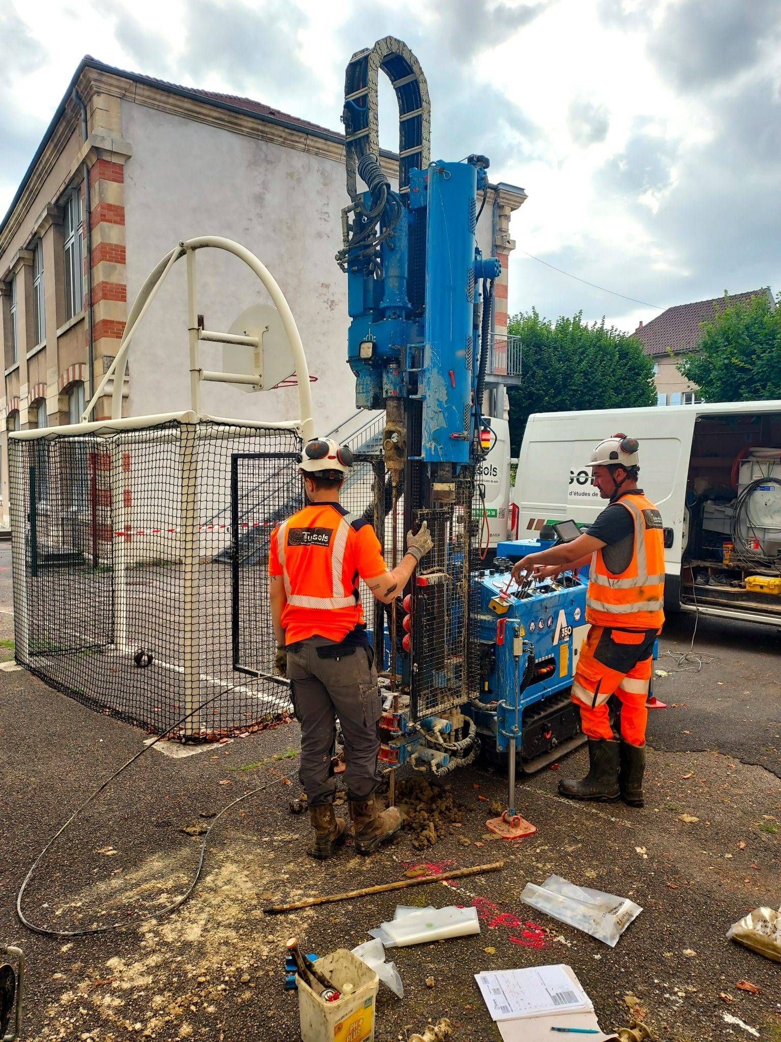 Une plate-forme de forage dans un champ enneigé. Une autre plate-forme et des ouvriers en gilet orange sont visibles à l'arrière-plan.
