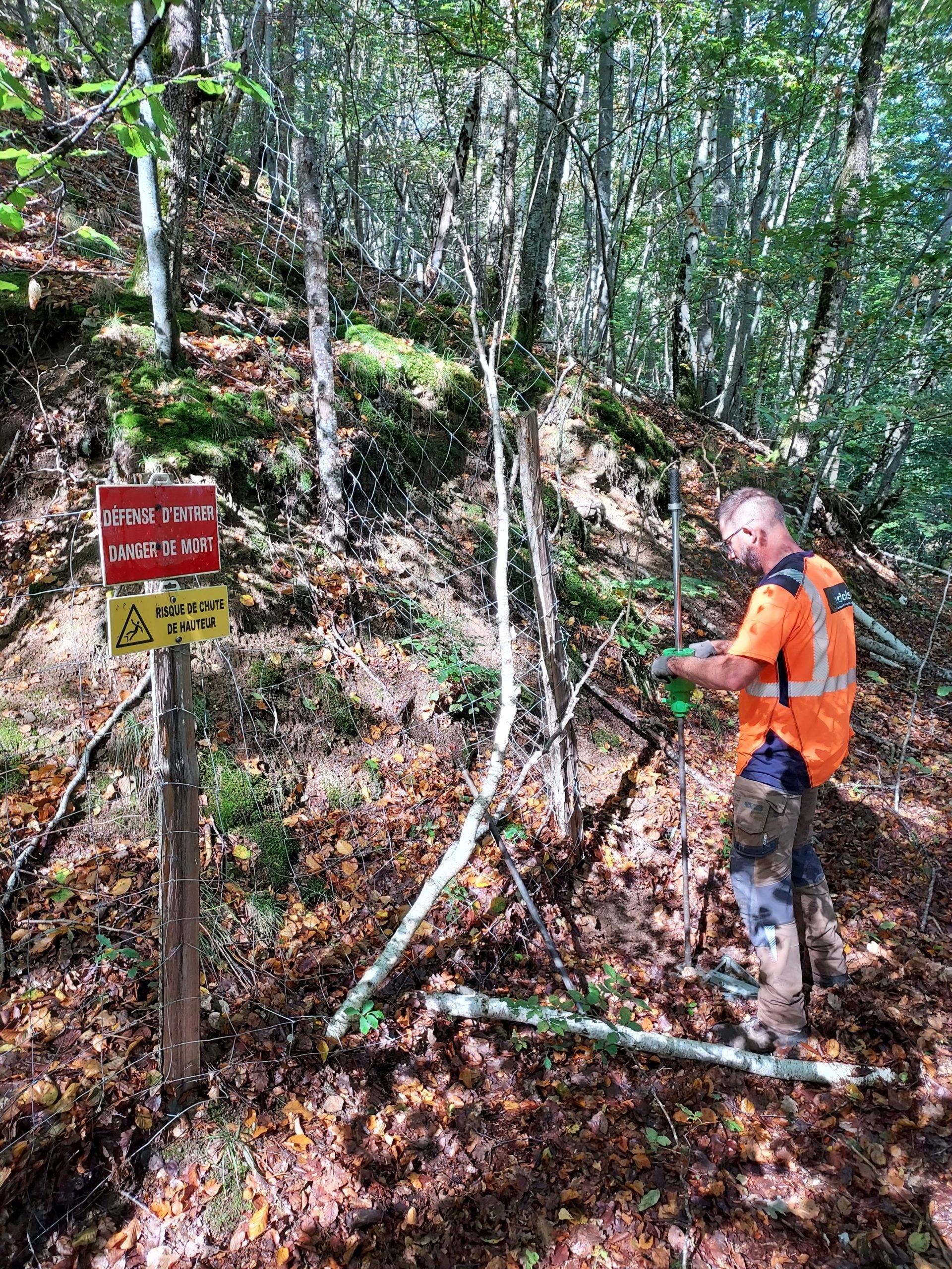 Un homme en gilet orange près de panneaux dans une forêt.