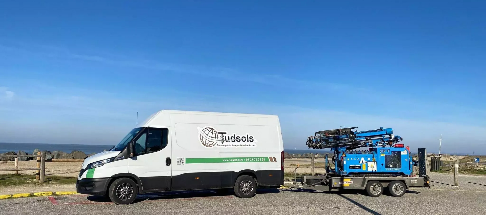 Camionnette blanche avec le logo de l'entreprise garée sur du gravier au bord de l'océan.