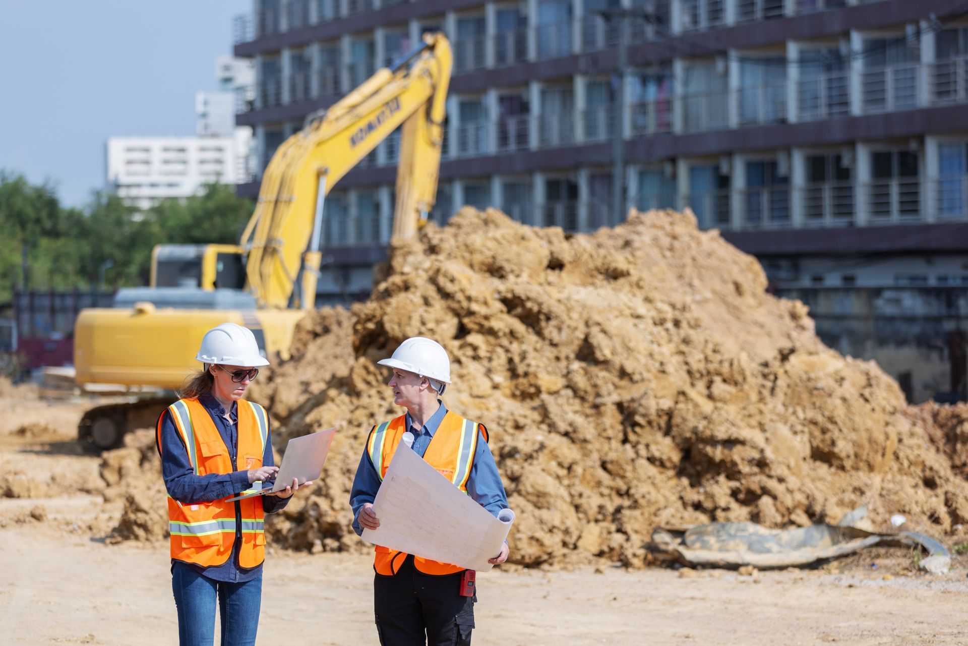 Deux ouvriers du bâtiment portant des gilets de sécurité et des casques de sécurité examinent des plans sur un chantier de construction.