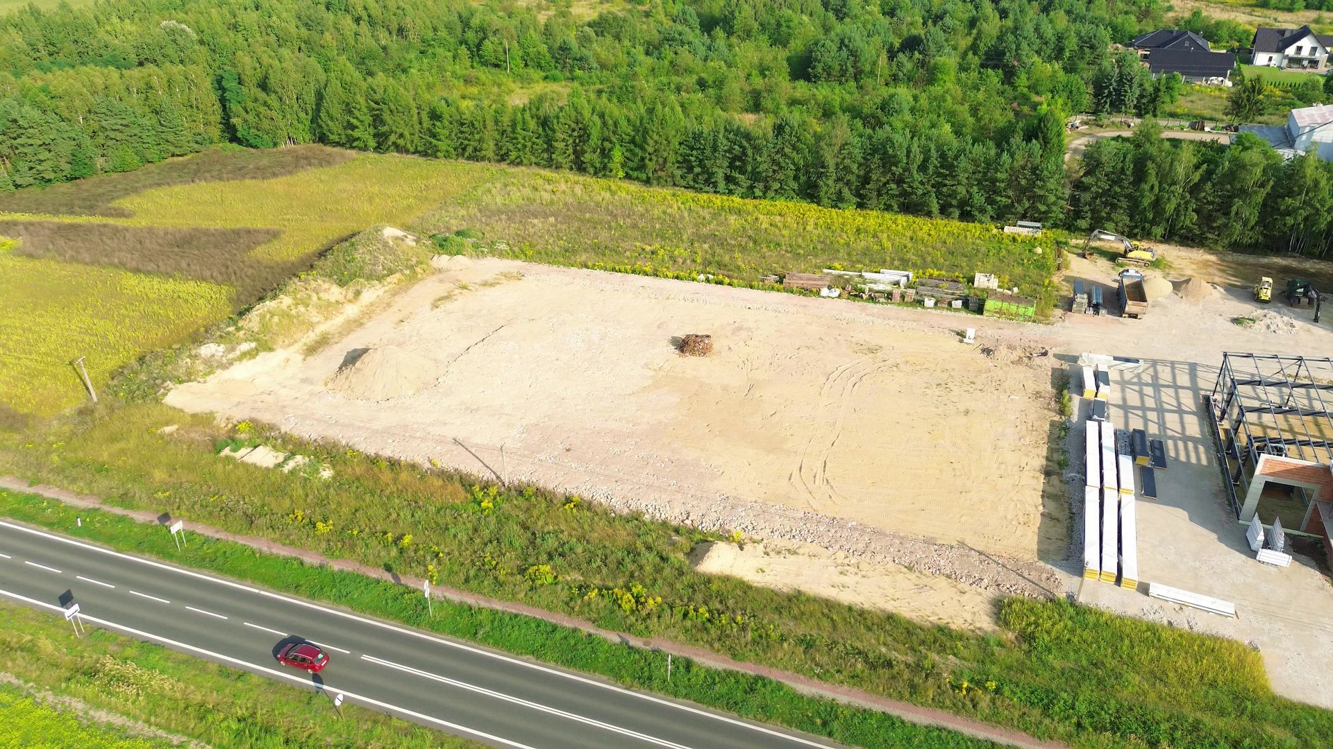 Vue aérienne d'un chantier de construction dégagé avec une route et une zone boisée en arrière-plan.