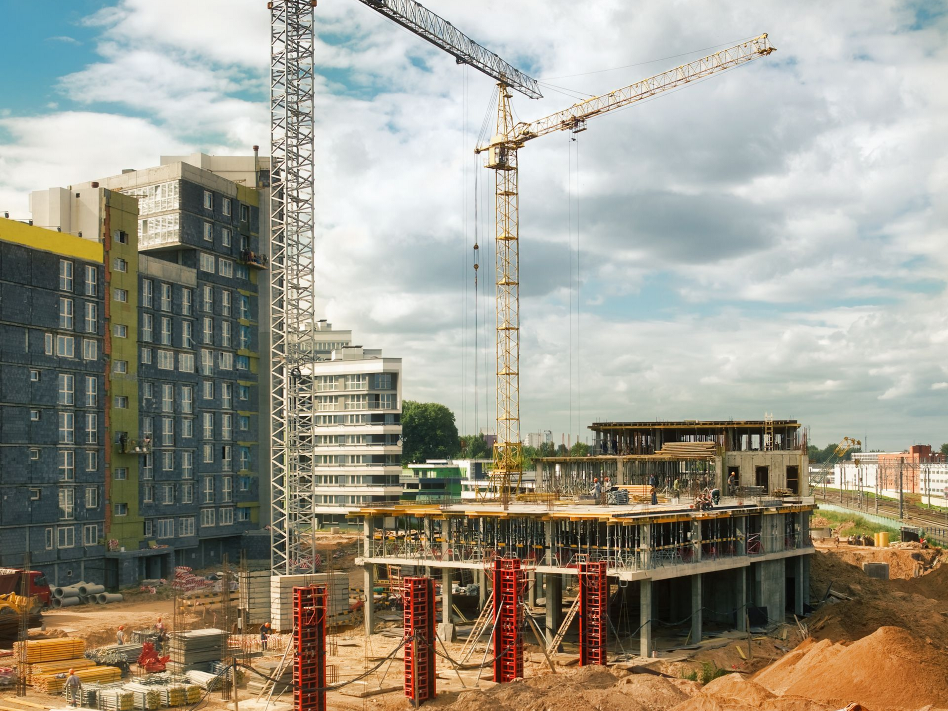 Chantier de construction avec grues ; bâtiments inachevés et terrain avec matériaux.