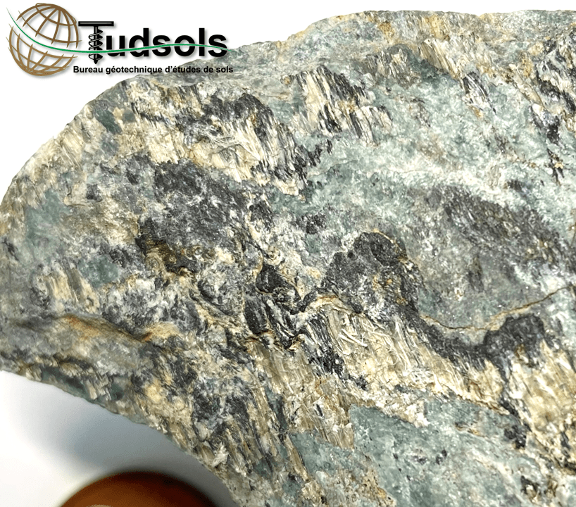 Gros plan d'une roche métamorphique feuilletée, montrant des couches de minéraux gris, noirs et bruns.