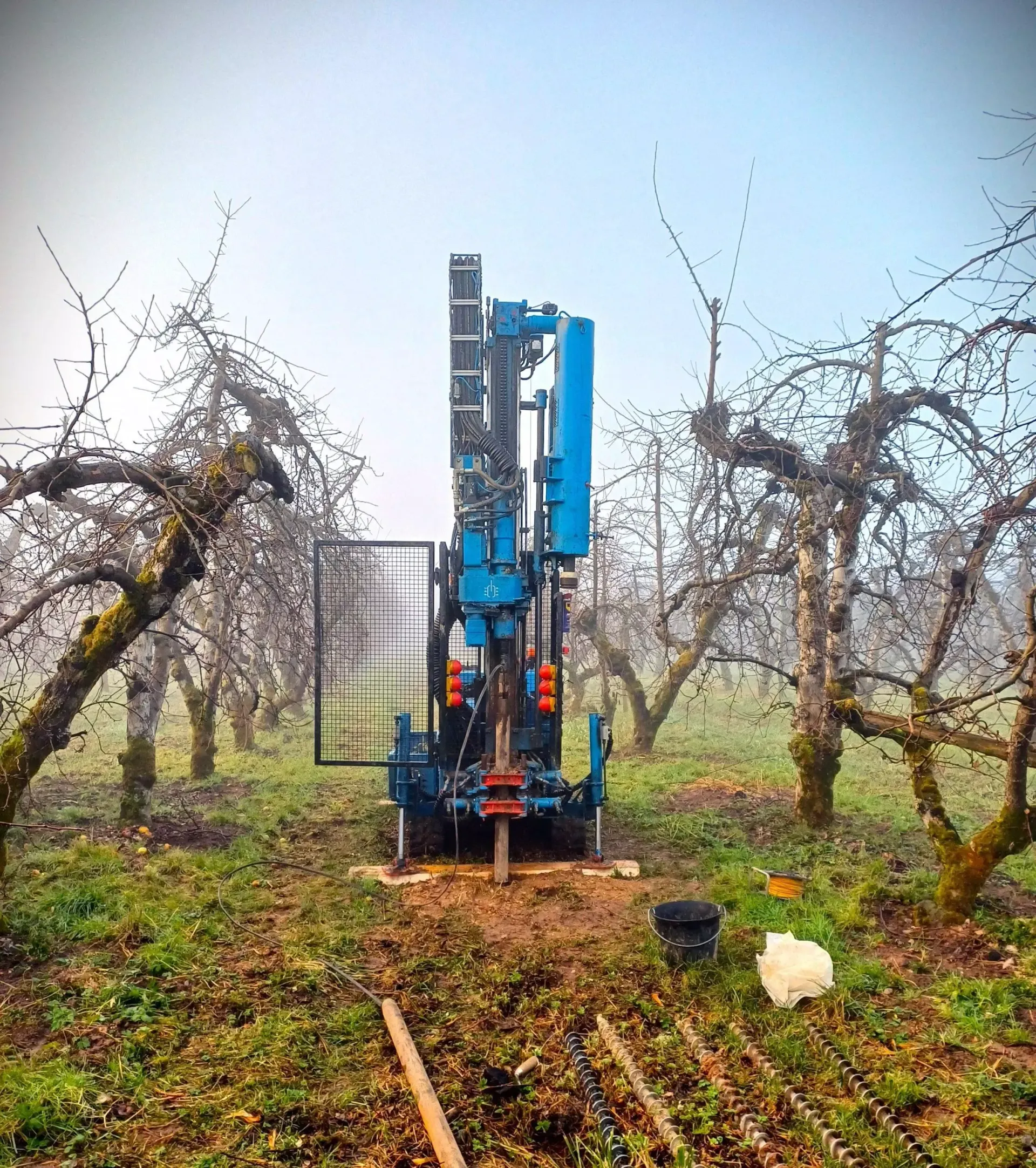 Foreuse bleue creusant un trou dans un verger.