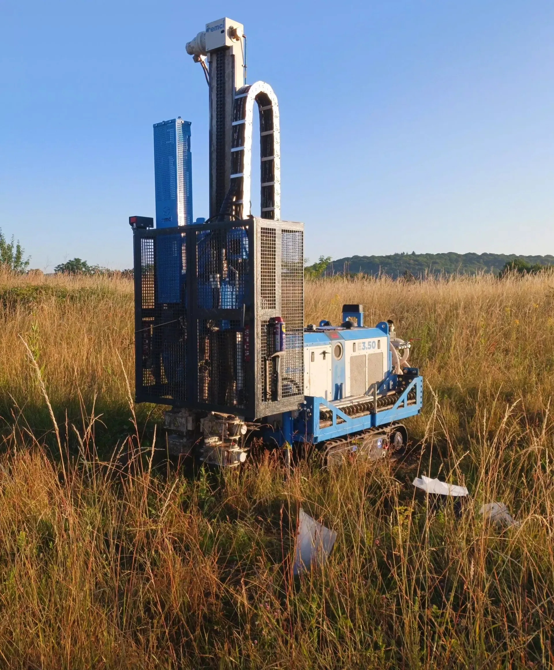 Plateforme de forage bleue et blanche dans un champ herbeux sous un ciel bleu.