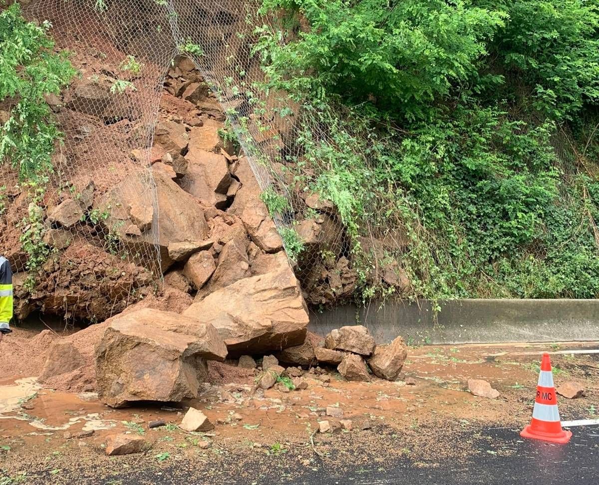 Éboulement sur une route, gros rochers et débris bloquant la voie, cône de sécurité présent.