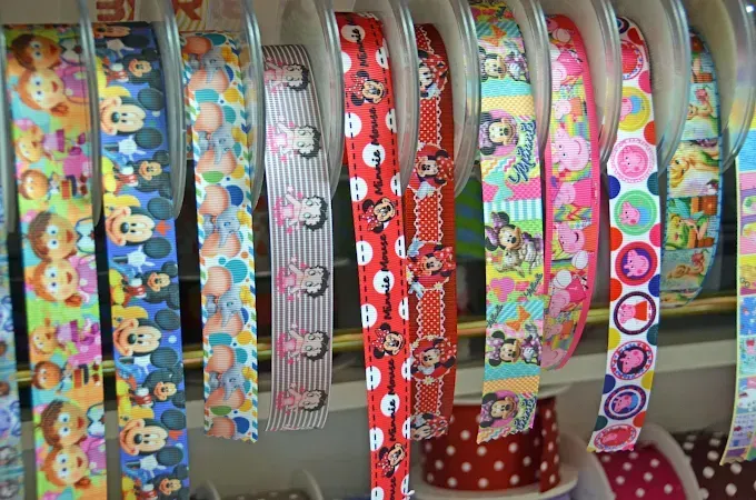 En una tienda, hileras de cintas decorativas de colores y estampados cuelgan verticalmente en estantes de exhibición.