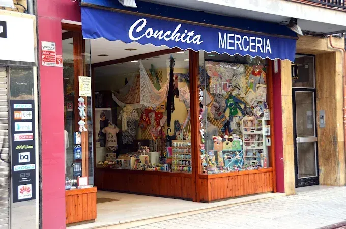 La fachada a pie de calle de Conchita Merceria, con un toldo azul y un escaparate repleto de artículos para manualidades.