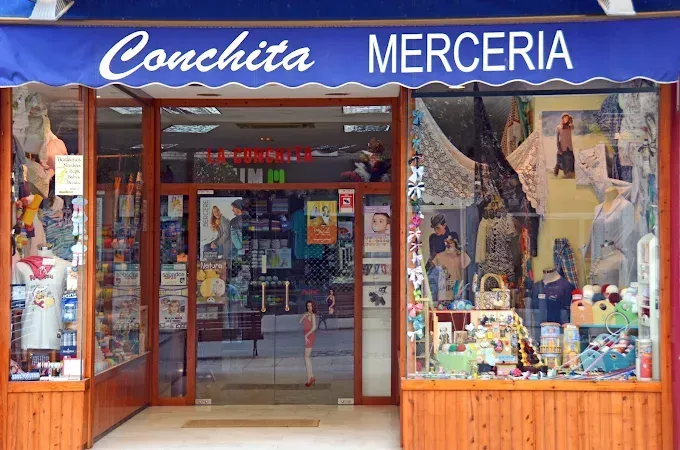 La fachada de Conchita Merceria, una pequeña tienda con un toldo azul y grandes escaparates repletos de artículos de costura.