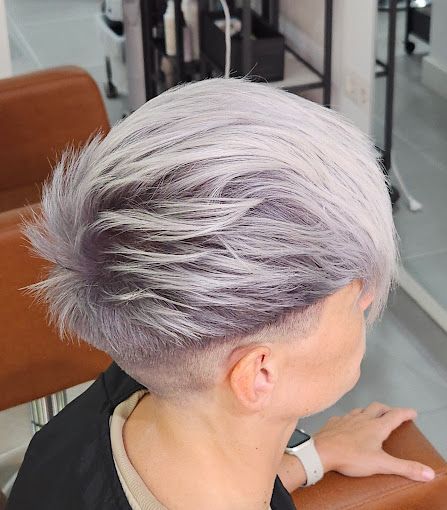 Una mujer con cabello corto y gris está sentada en una silla en un salón.