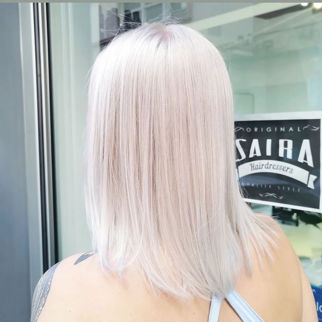 Una mujer con cabello blanco está parada frente a un cartel que dice saira