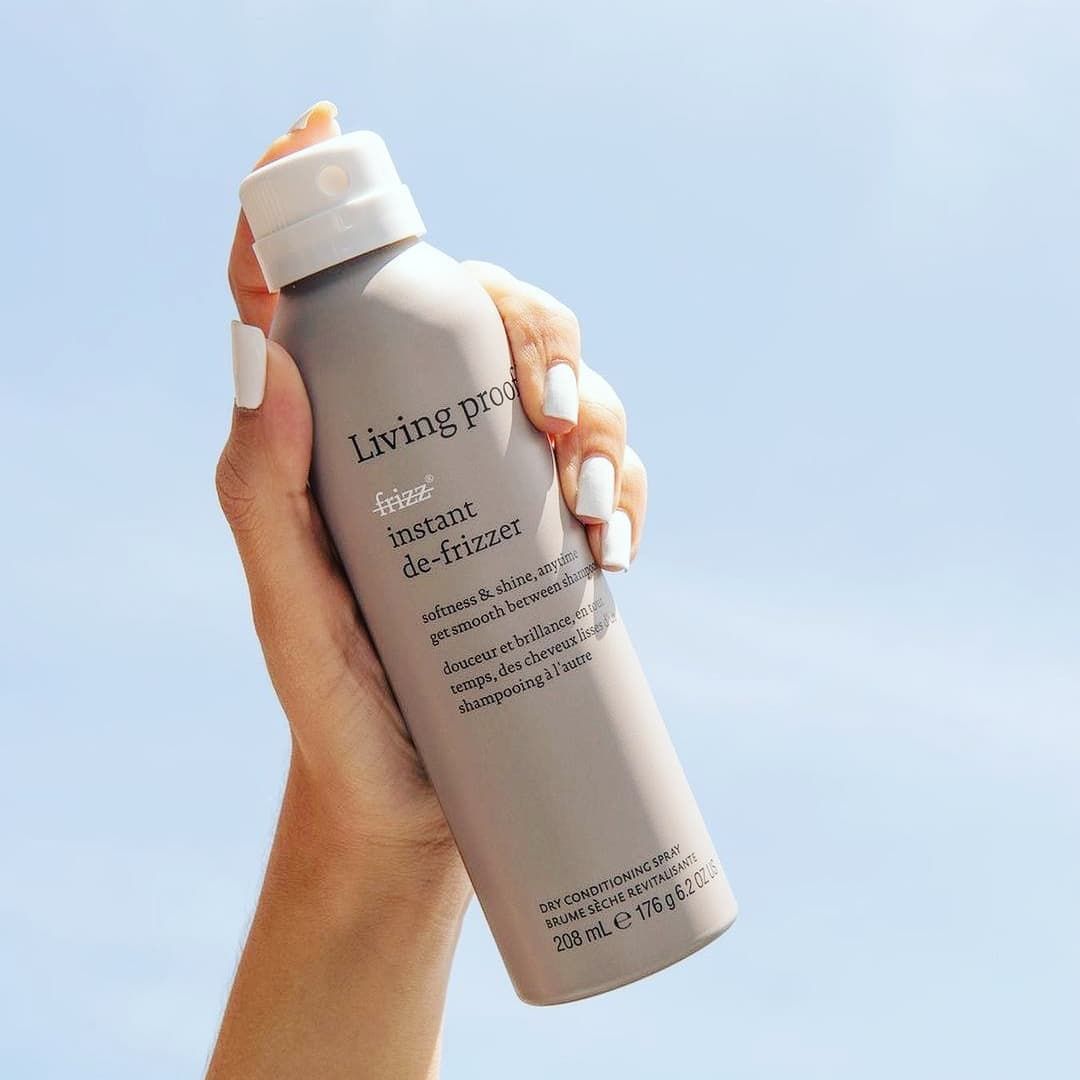 Una mujer sostiene una botella de spray para el cabello Living Proof en su mano.