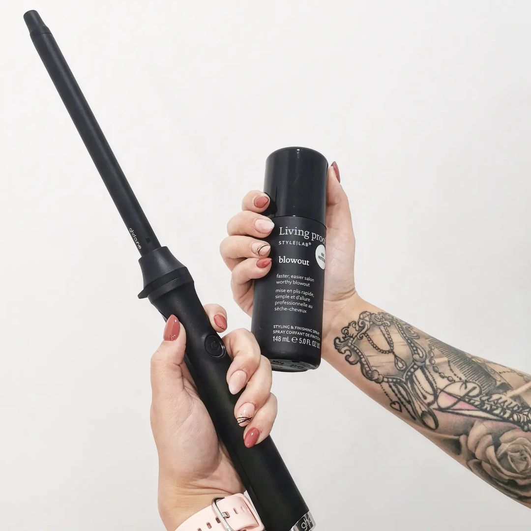 Una mujer con un tatuaje en el brazo sostiene una botella de producto para el cabello.