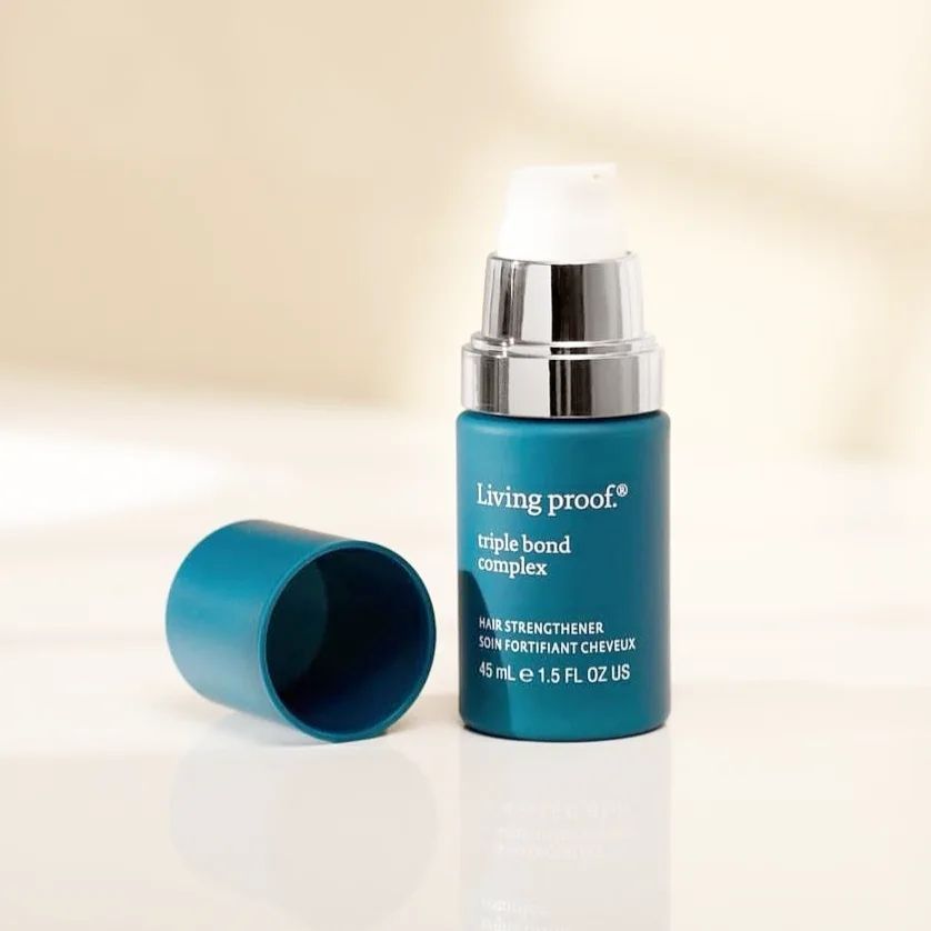 Una botella de complejo de triple enlace Living Proof se encuentra sobre una mesa.