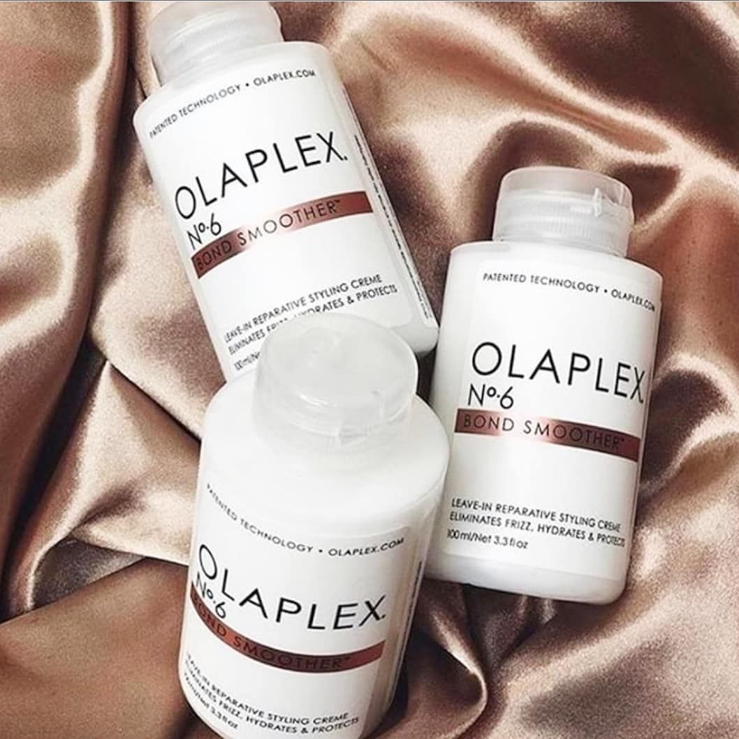 Tres botellas de productos para el cabello Olaplex están sobre un paño rosa.